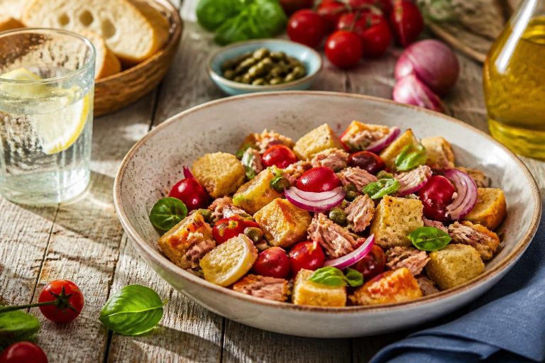Panzanella croccante con tonno servita in una ciotola rustica, con pomodori datterini, basilico fresco e pane tostato dorato, fotografata dall'alto su tavola di legno chiaro