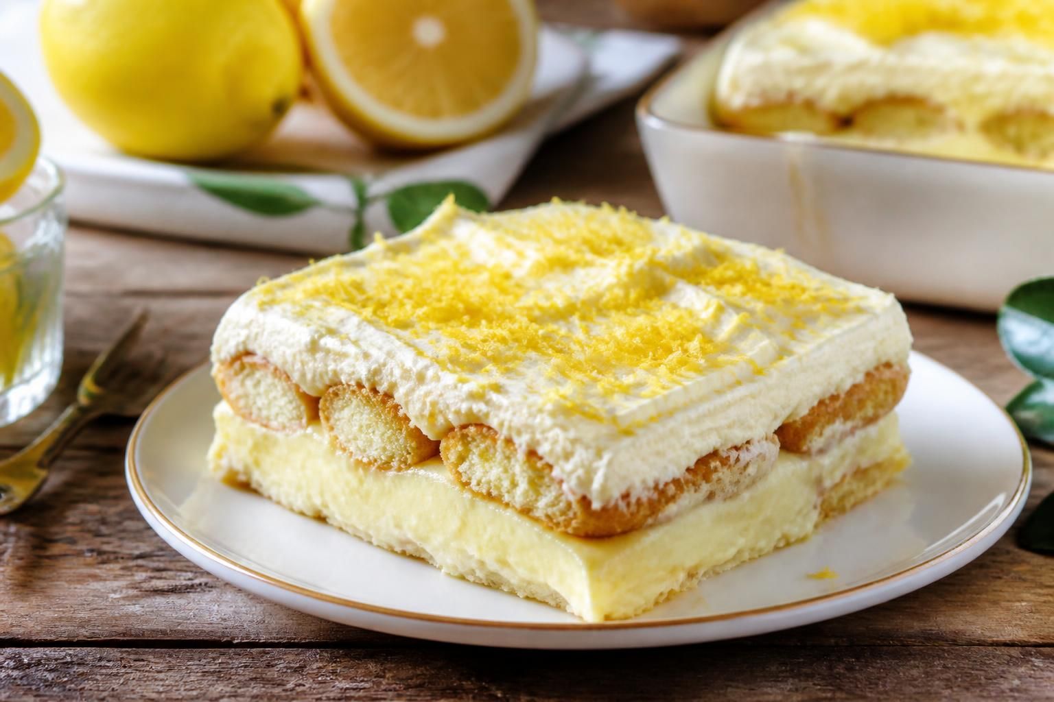 Tiramisù al limone senza uova servito in una pirofila, con strati di crema al mascarpone e savoiardi, decorato con scorza di limone grattugiata e foglioline di menta fresca
