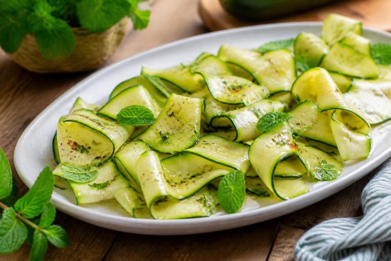 Zucchine marinate a crudo in un piatto bianco, condite con olio extravergine, limone, aglio e menta fresca